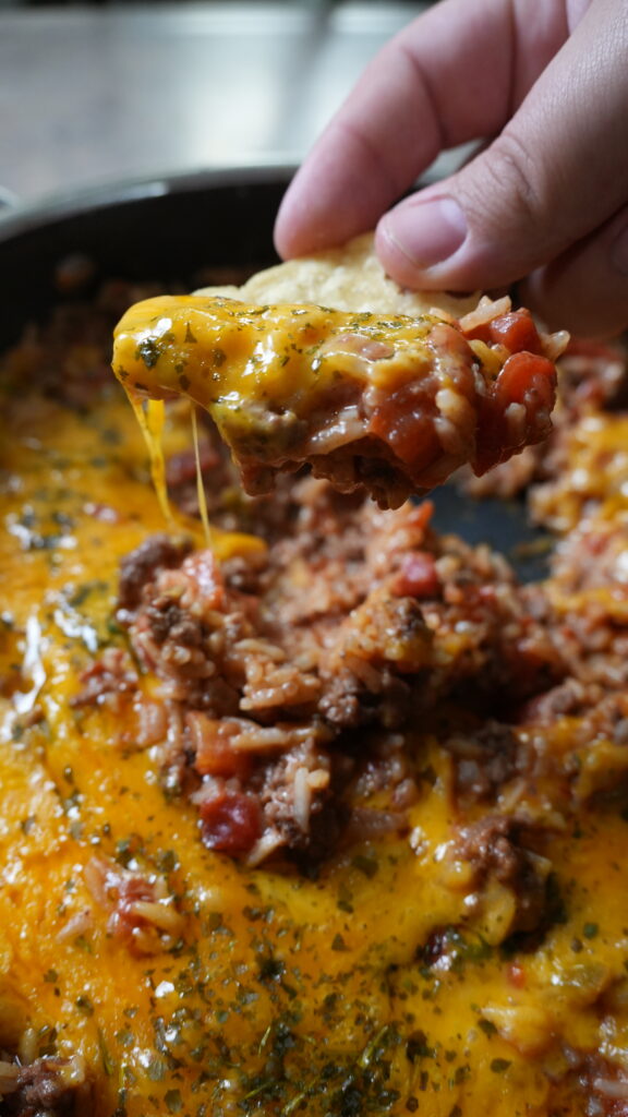 pan of cheesy taco rice with a tortilla chip dipping into it