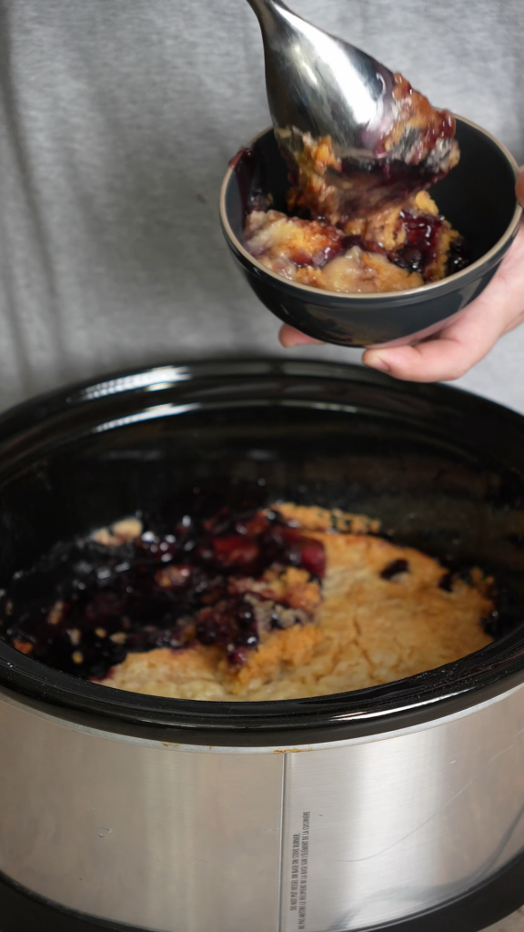 Justin dishing up a bowl of blueberry dump cake from a crockpot
