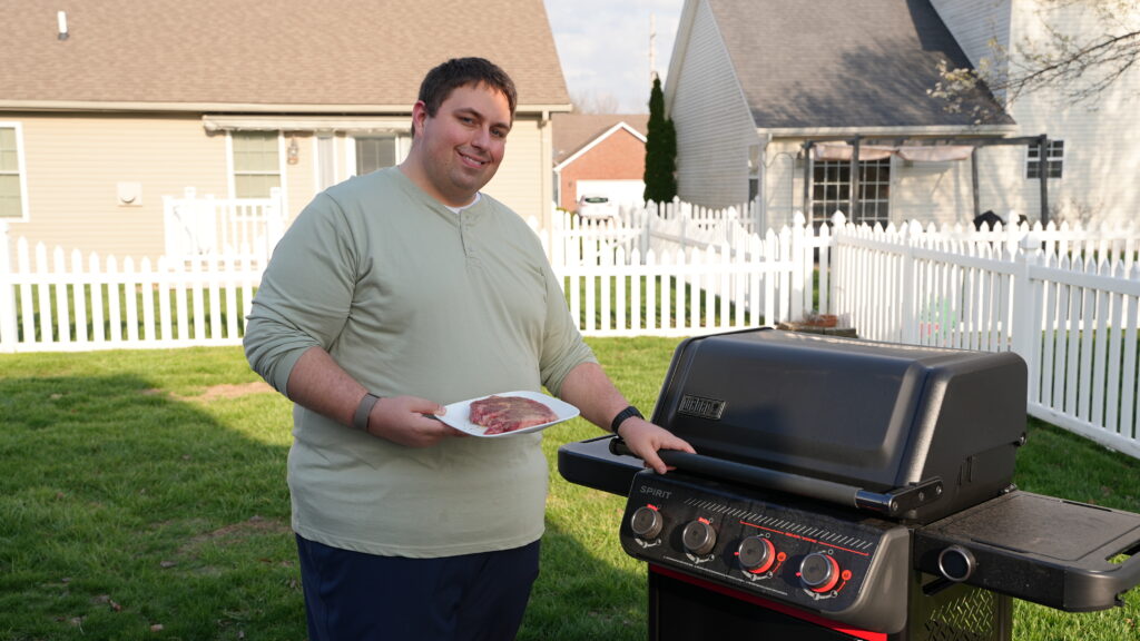 Justin standing by a grill with steak on plate, getting ready to grill