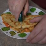 quesadilla on plate being cut with a pizza cutter
