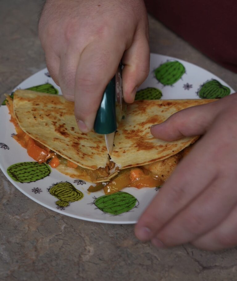 quesadilla on plate being cut with a pizza cutter
