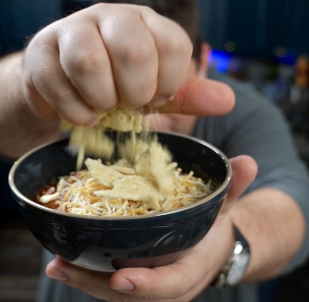 adding crushed crackers to bowl of chili